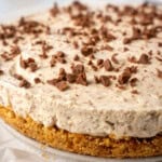 Close-up of a no-bake Baileys cheesecake with a thick creamy filling on a golden biscuit base, topped with chopped chocolate pieces.