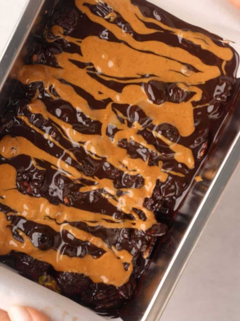 Loaf pan filled with melted dark chocolate and berries, drizzled with smooth peanut butter on top.
