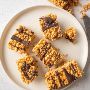 Overhead photo of sliced protein crisp bars on a white plate, drizzled with dark chocolate and scattered crumbs around the edges.