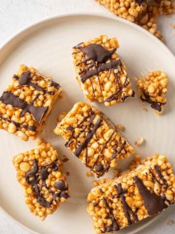 Overhead photo of sliced protein crisp bars on a white plate, drizzled with dark chocolate and scattered crumbs around the edges.