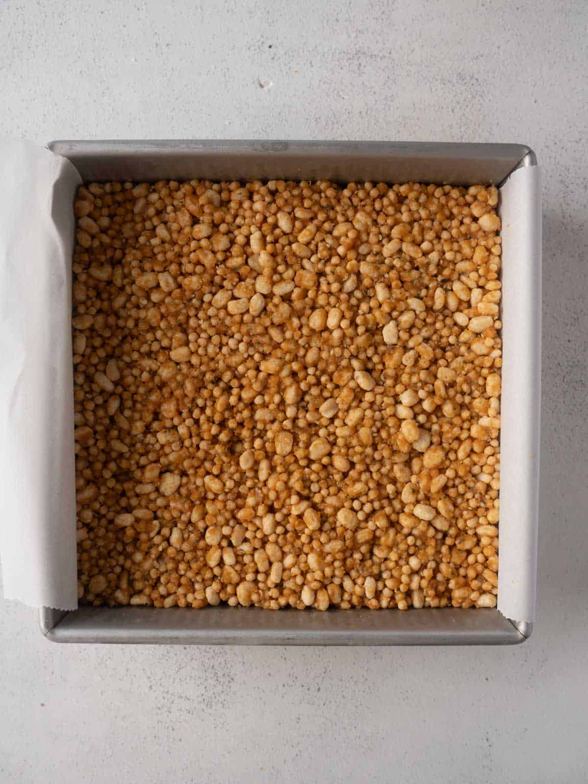 Protein crisp bar mixture pressed firmly into a parchment-lined square pan before chilling.