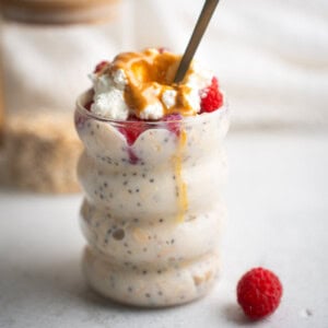 high protein overnight oats in a glass jar with a spoon sticking out and a raspberry in the foreground.