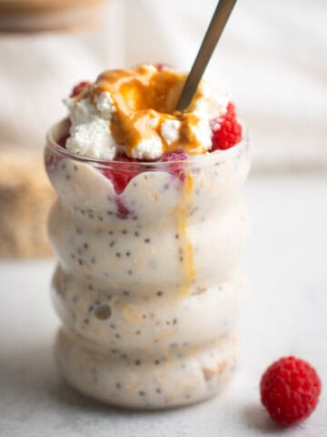 high protein overnight oats in a glass jar with a spoon sticking out and a raspberry in the foreground.