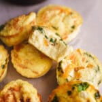 Golden brown egg bites filled with spinach, cheese, and vegetables, stacked on parchment paper with one cut open to show the fluffy texture inside.