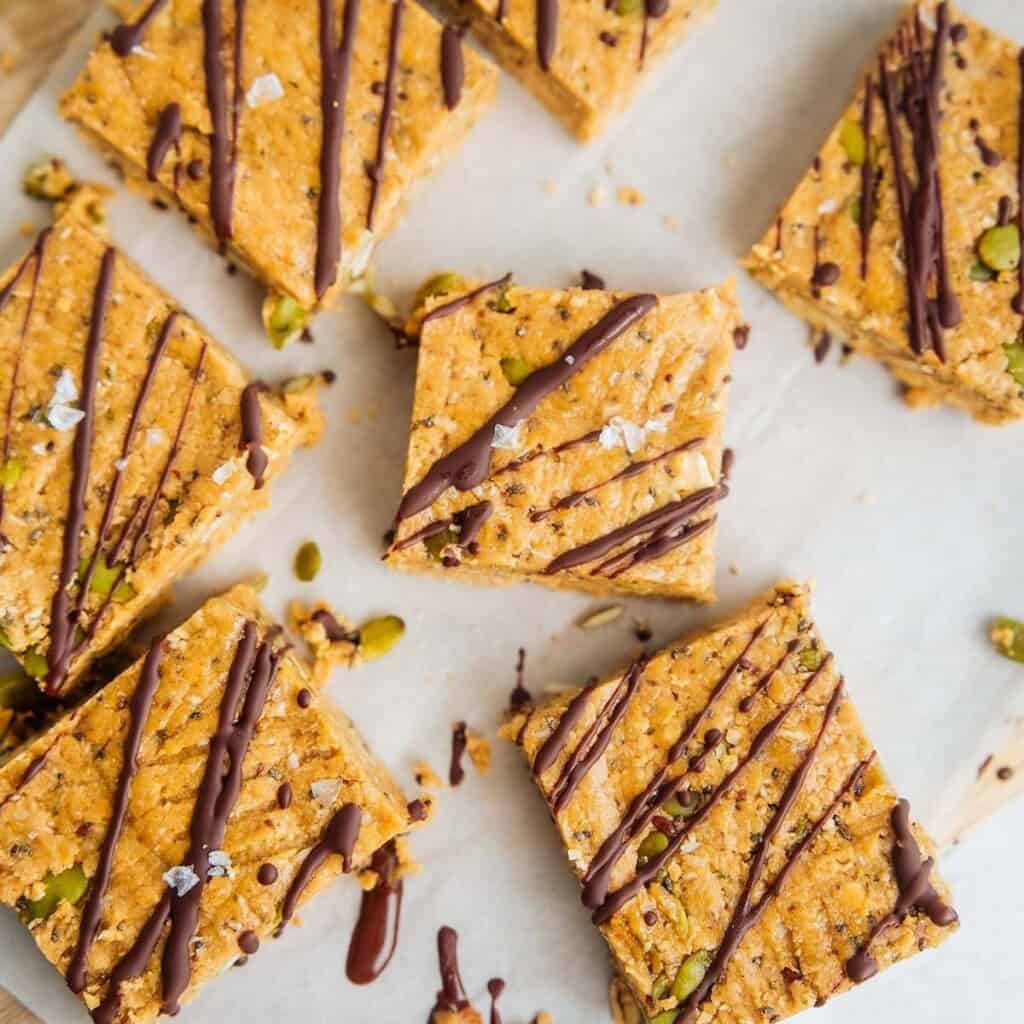 Homemade oat breakfast bars topped with a drizzle of melted chocolate and sprinkled with flaky sea salt, cut into squares and arranged on parchment paper.