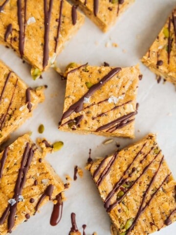 Homemade oat breakfast bars topped with a drizzle of melted chocolate and sprinkled with flaky sea salt, cut into squares and arranged on parchment paper.