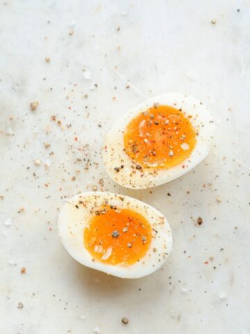 Soft-boiled egg halves sprinkled with cracked black pepper and sea salt on a light marble surface.
