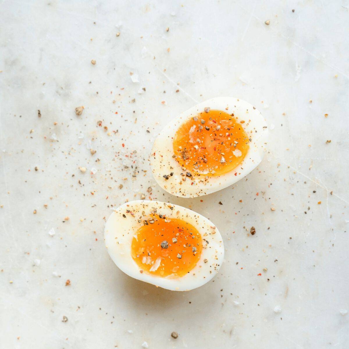 Soft-boiled egg halves sprinkled with cracked black pepper and sea salt on a light marble surface.