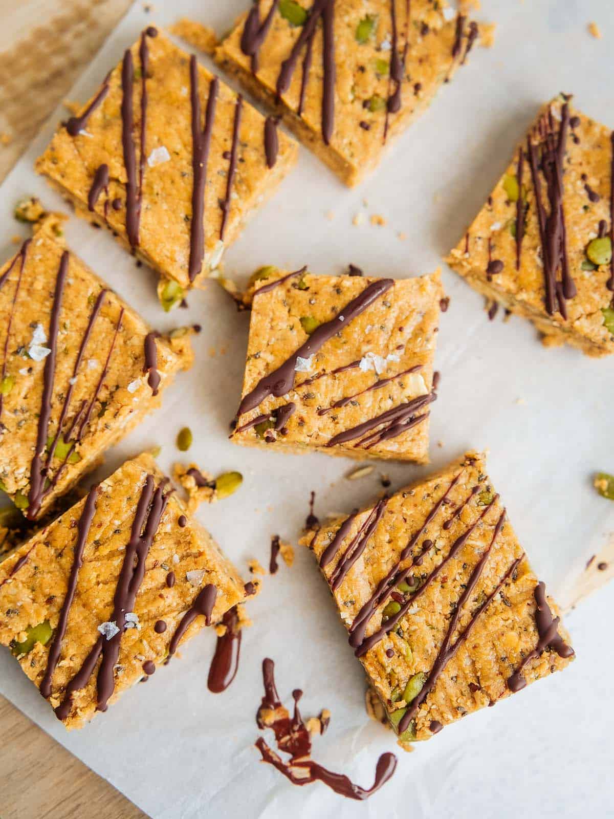 Homemade oat breakfast bars topped with a drizzle of melted chocolate and sprinkled with flaky sea salt, cut into squares and arranged on parchment paper.