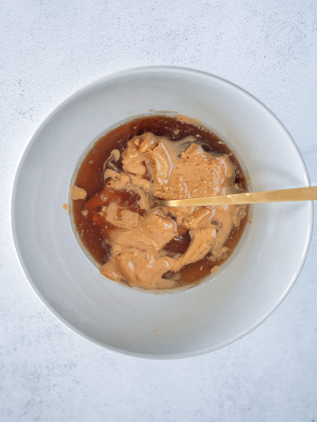 Mixing bowl with peanut butter and maple syrup before combining, the wet ingredients for oat breakfast bars.