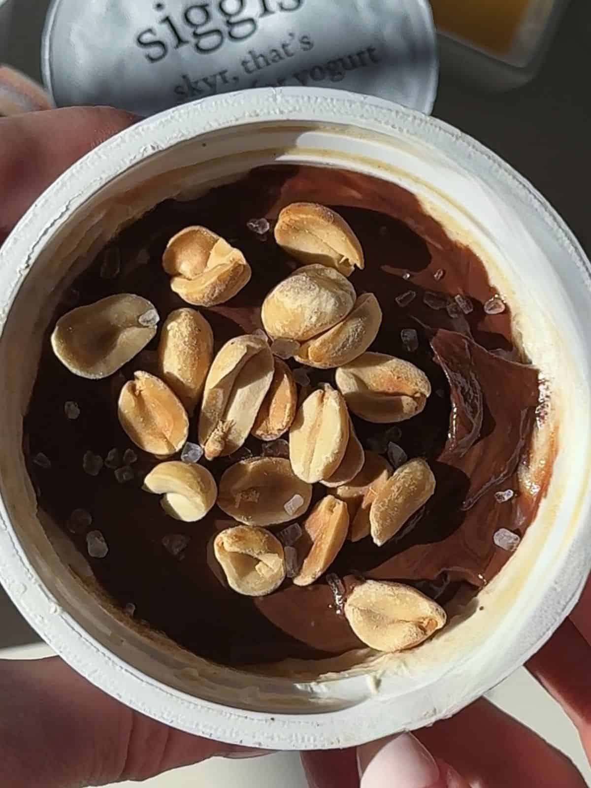 High-protein Snickers yogurt cup topped with a chocolate layer, roasted peanuts and flaky sea salt.