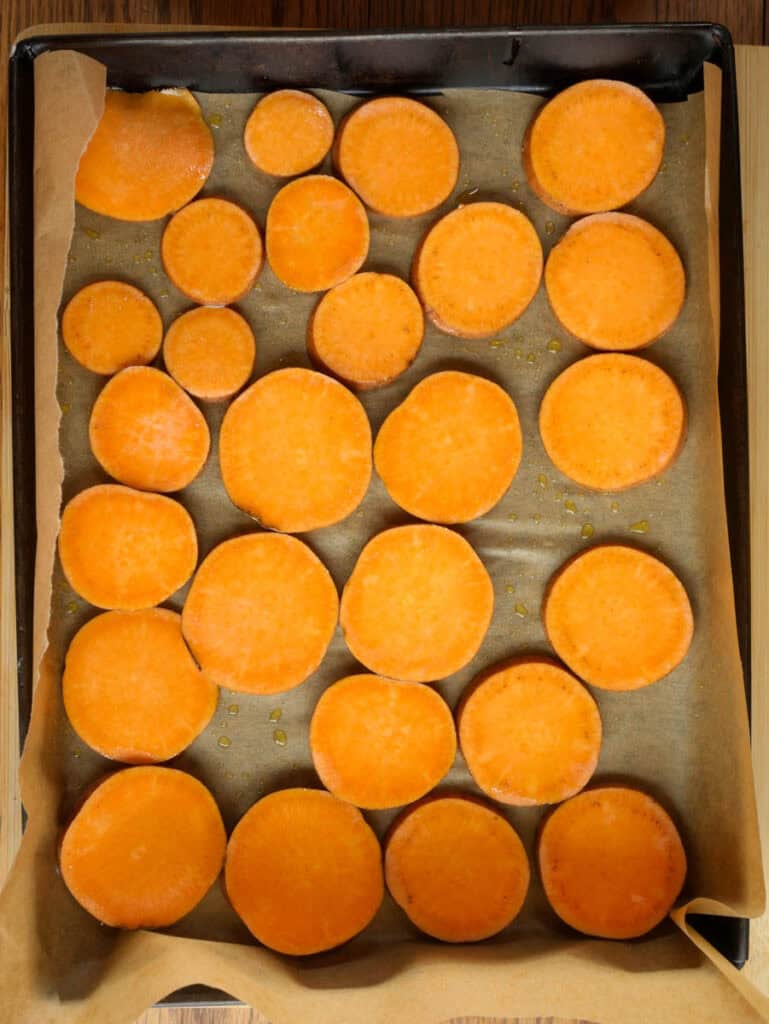 Uncooked sweet potato rounds arranged on a parchment-lined baking tray, ready for roasting.
