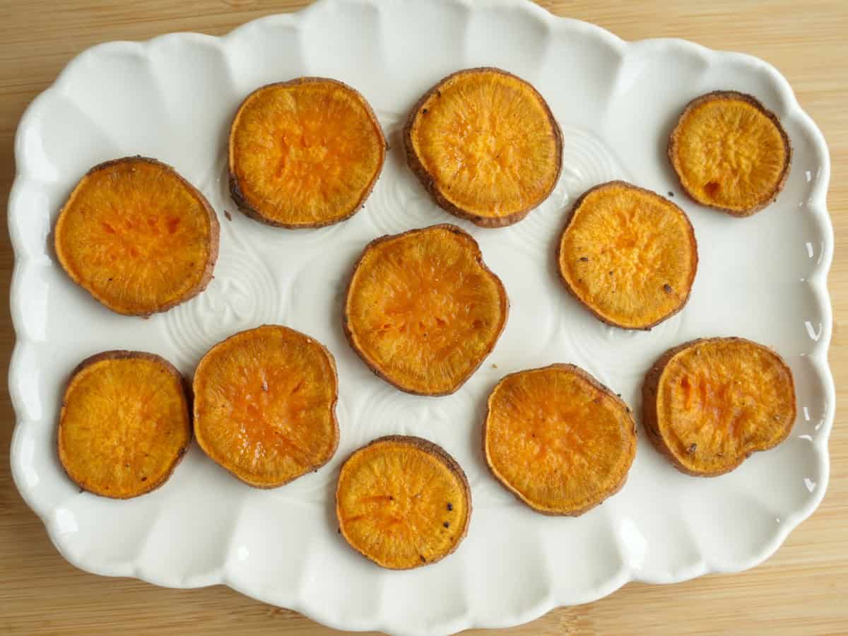 Golden roasted sweet potato rounds fresh out of the oven on a white plate, slightly caramelized and crispy on the edges.