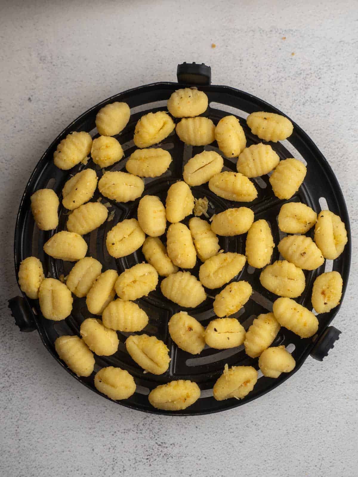 Seasoned gnocchi spread evenly in an air fryer basket before cooking.