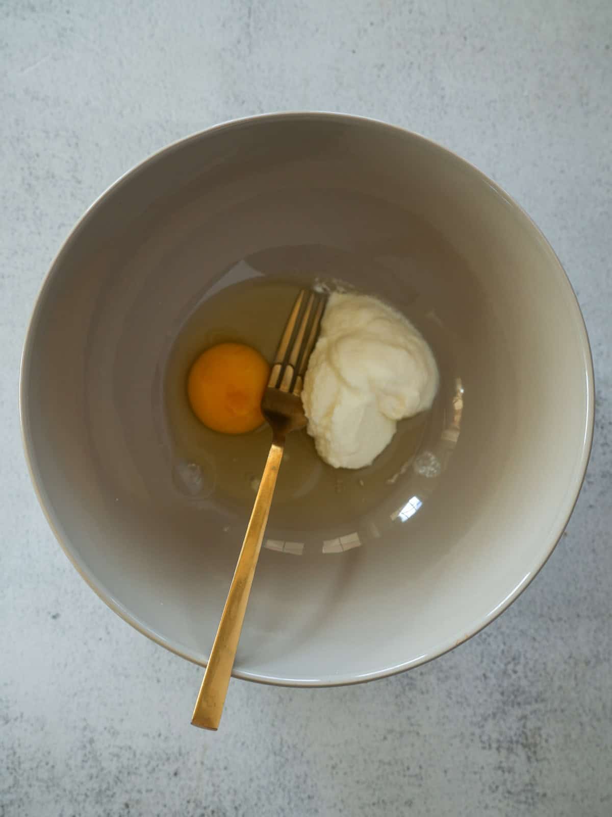 Large mixing bowl with a whole raw egg and a scoop of ricotta cheese, with a gold fork resting inside.