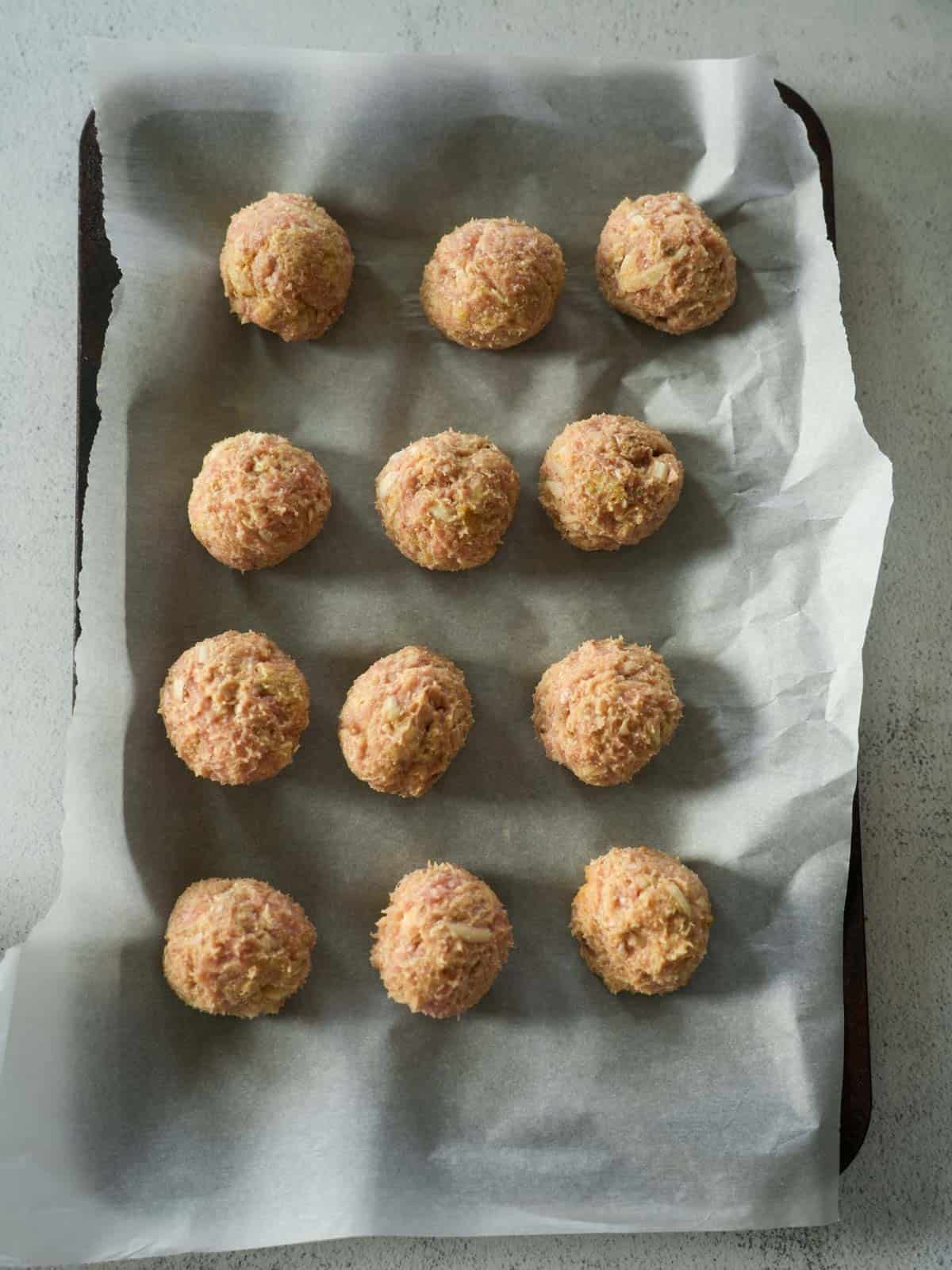 Uncooked turkey meatballs arranged in four rows on a parchment-lined baking sheet, ready for air frying.