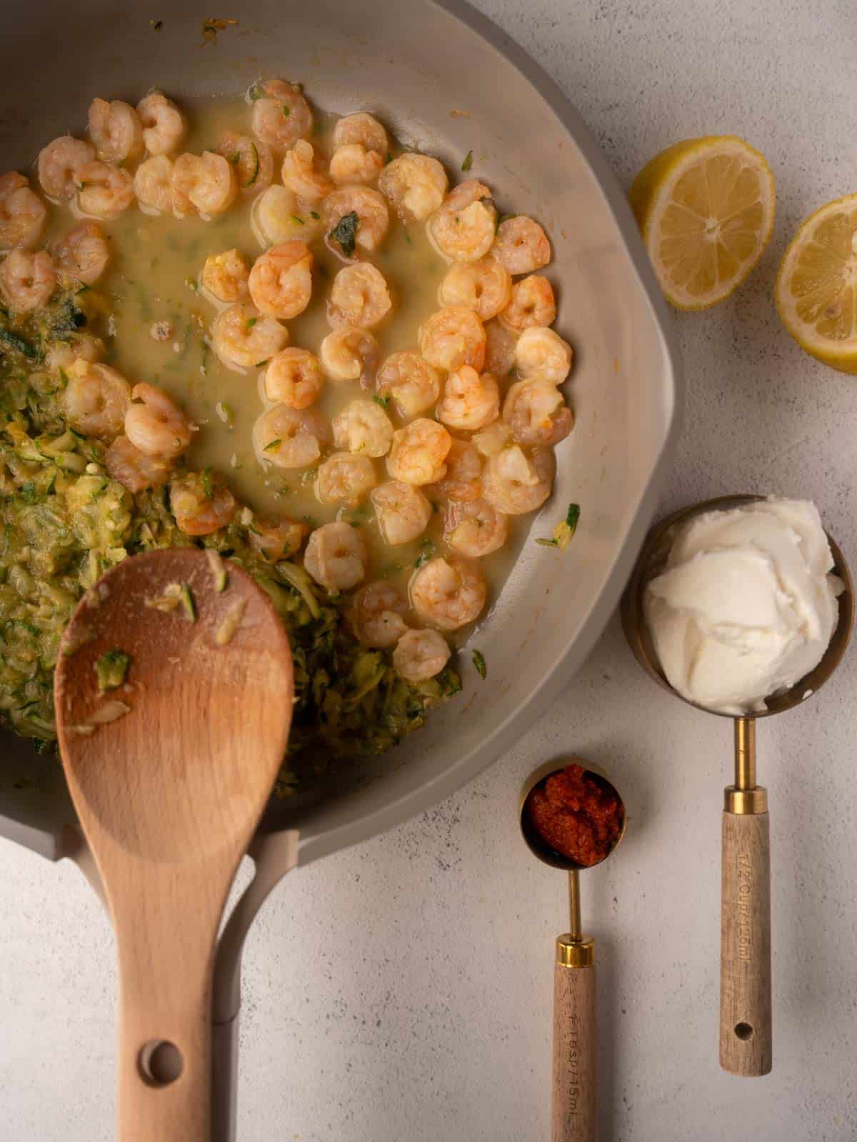 Fourth step is creating the creamy sauce for the Pesto Ricotta Pasta recipe. The image shows the cooked shrimp and zucchini in the skillet, with measured portions of ricotta cheese and pesto ready to be added.