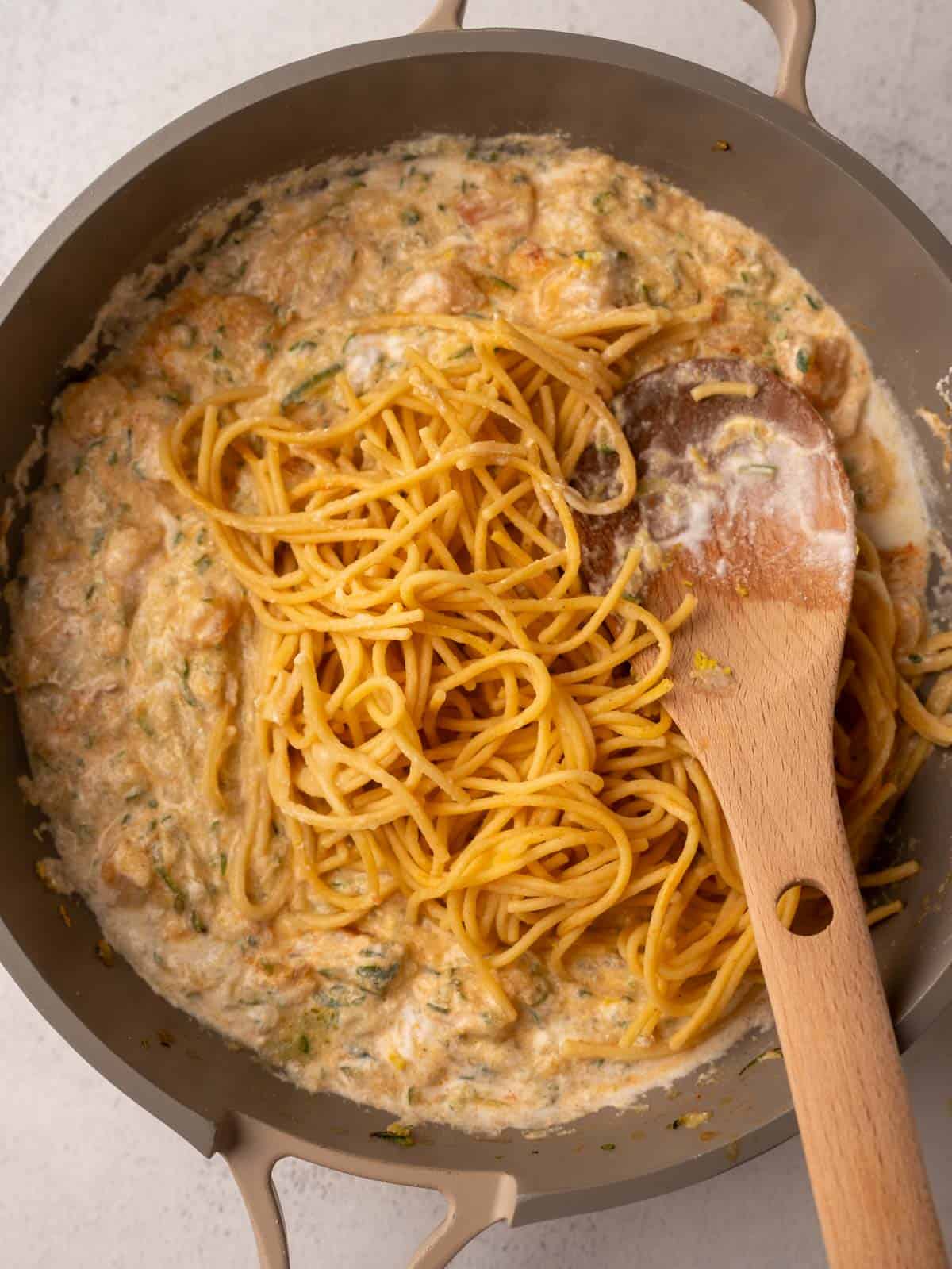 The last step is showing cooked spaghetti being stirred into the skillet with the rich Pesto Ricotta Pasta with Shrimp sauce, creating the finished, balanced meal.