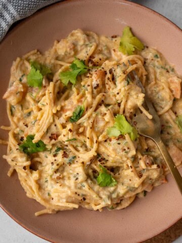 A pink bowl of creamy pesto ricotta pasta with shrimp, garnished with fresh herbs and chili flakes.
