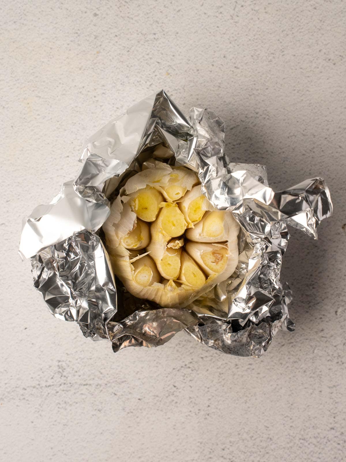 Garlic cloves, drizzled with olive oil, are securely wrapped in aluminum foil, ready for roasting to enhance the tomato carrot soup flavor.