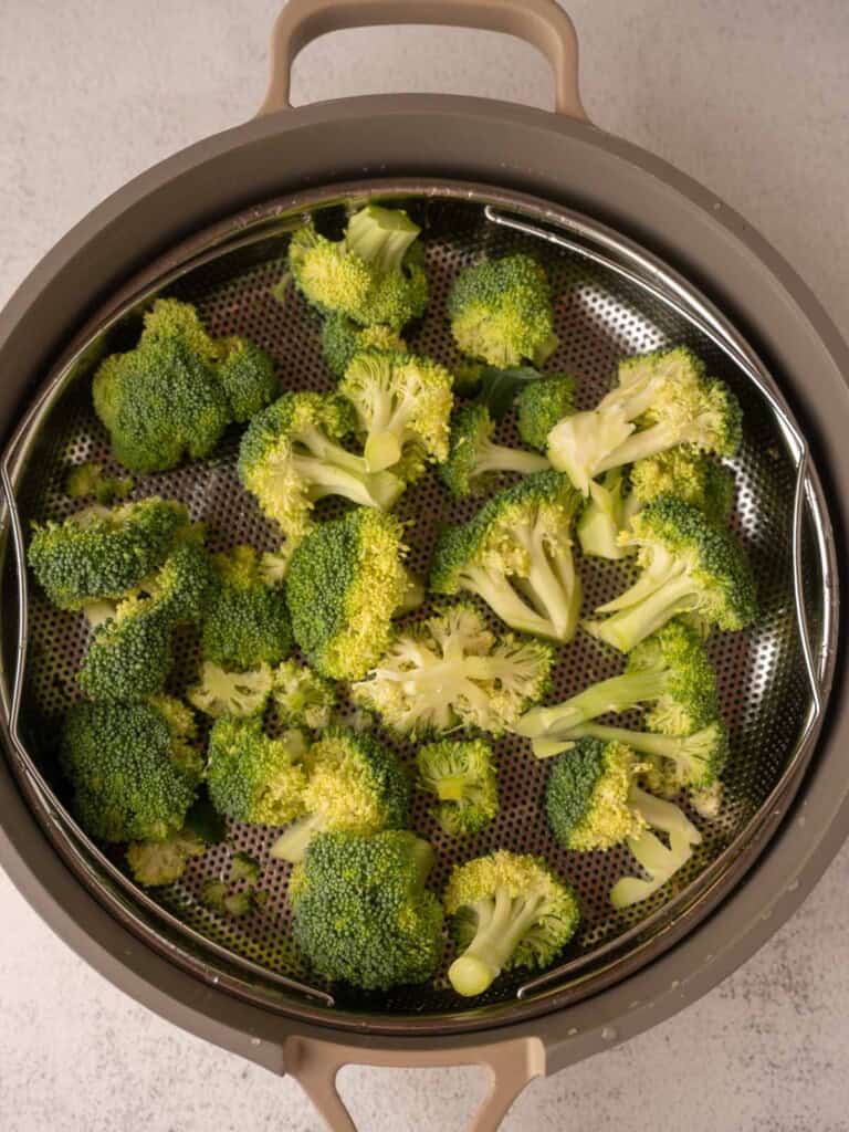 A top-down view of fresh broccoli florets in a stainless steel steamer basket, ready for steaming in a pot for a healthy meal.