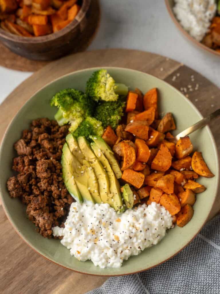 A close-up of a high-protein sweet potato and ground beef bowl, assembled with roasted sweet potatoes, seasoned beef, broccoli, cottage cheese, and sliced avocado.