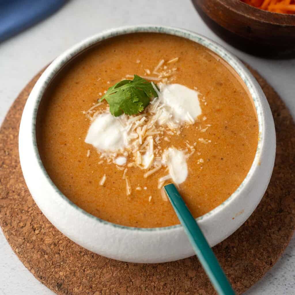 Creamy tomato carrot soup with a dollop of ricotta, shredded Parmesan, and fresh basil, served in a white bowl.