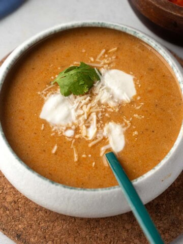 Creamy tomato carrot soup with a dollop of ricotta, shredded Parmesan, and fresh basil, served in a white bowl.