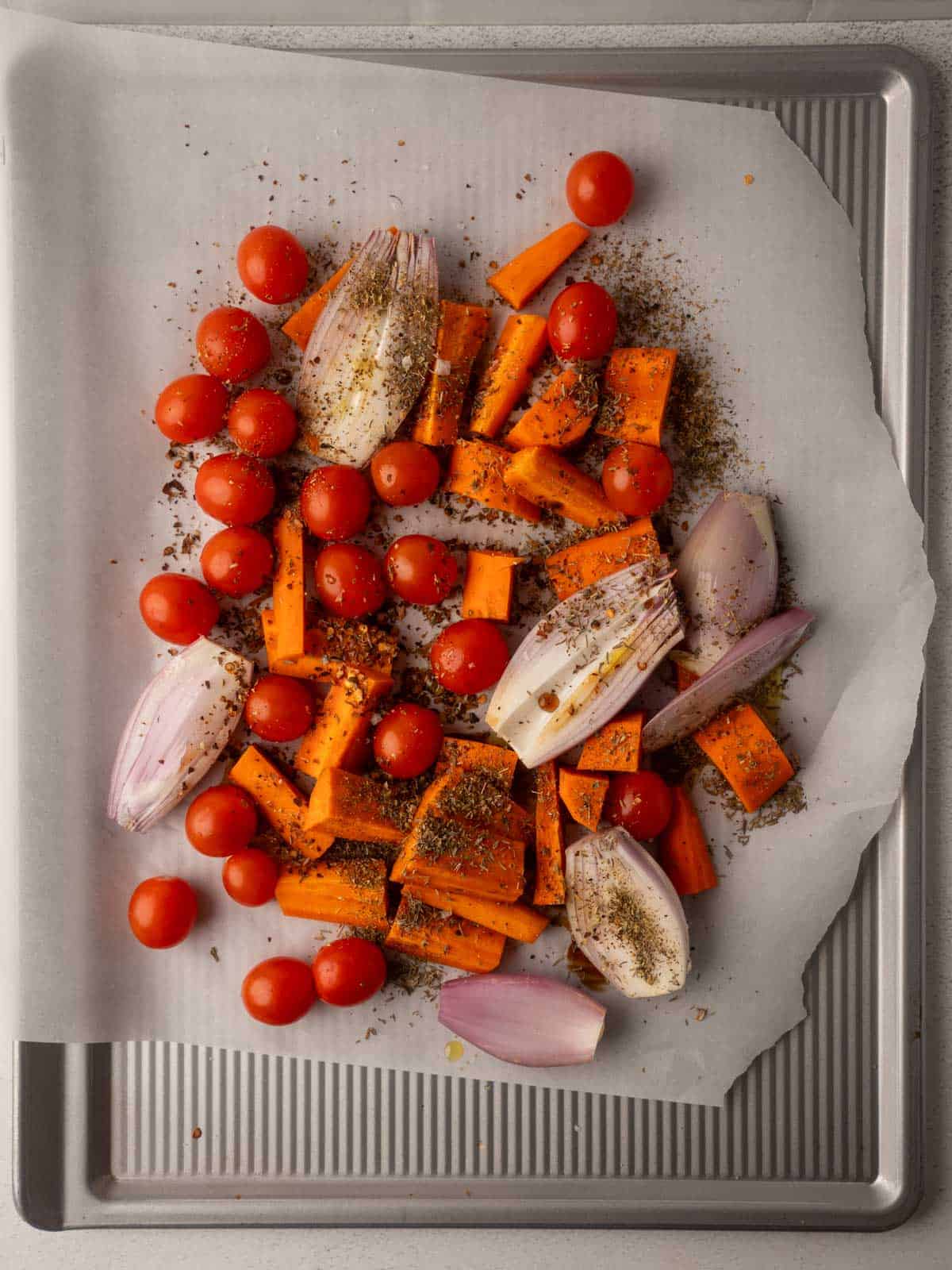 A baking sheet holds roasted cherry tomatoes, carrots, and shallots, showing prepped vegetables for a healthy tomato carrot soup base.