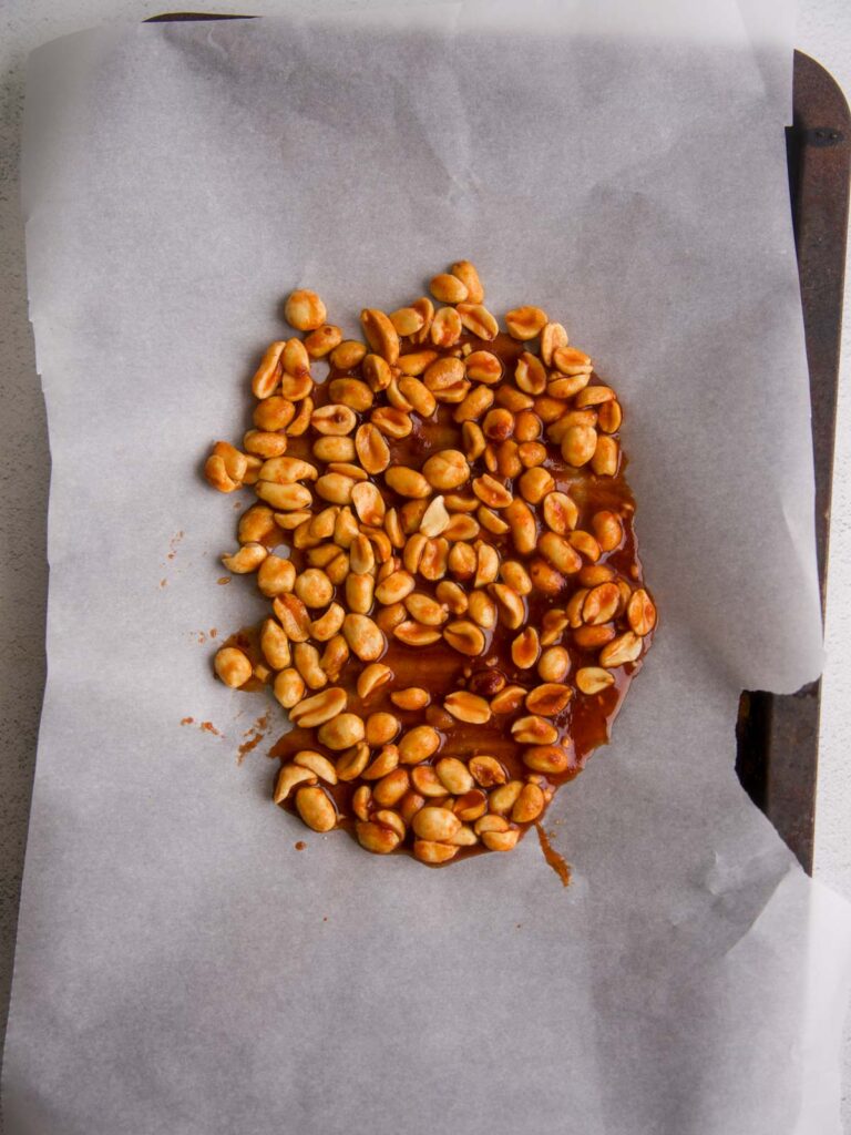 Honey-sriracha coated peanuts cooling on a parchment-lined baking tray for a spicy chicken salad.