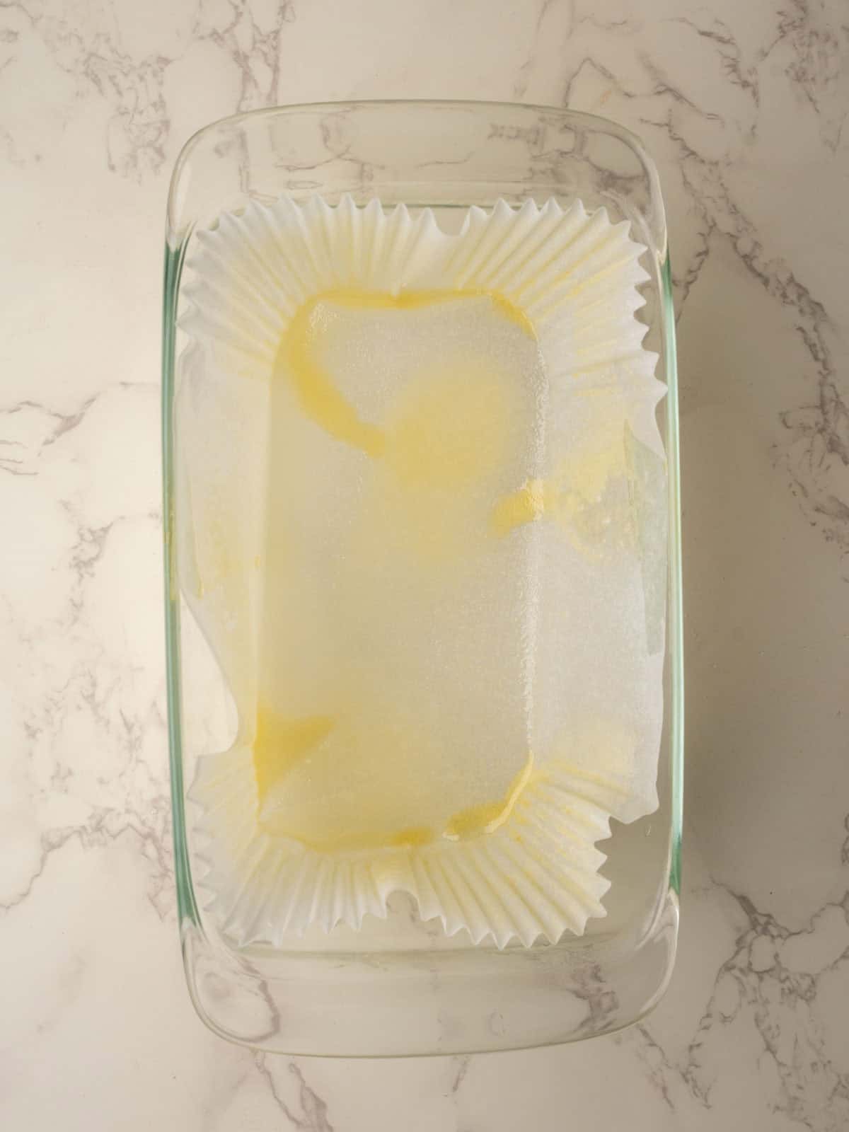 Glass loaf pan lined with parchment paper brushed with melted butter, ready for the brown bread batter.