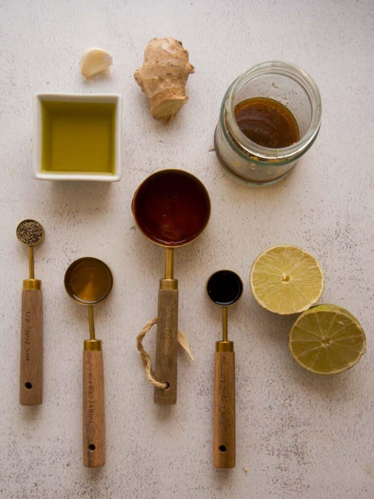 Overhead view of sauce ingredients including ginger, garlic, lime, soy sauce, sesame oil, honey, and sriracha arranged neatly on a light countertop.