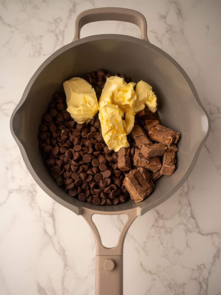 Saucepan with chocolate chips, butter, and chopped Mars bars being melted together as the base for rocky road with Maltesers.