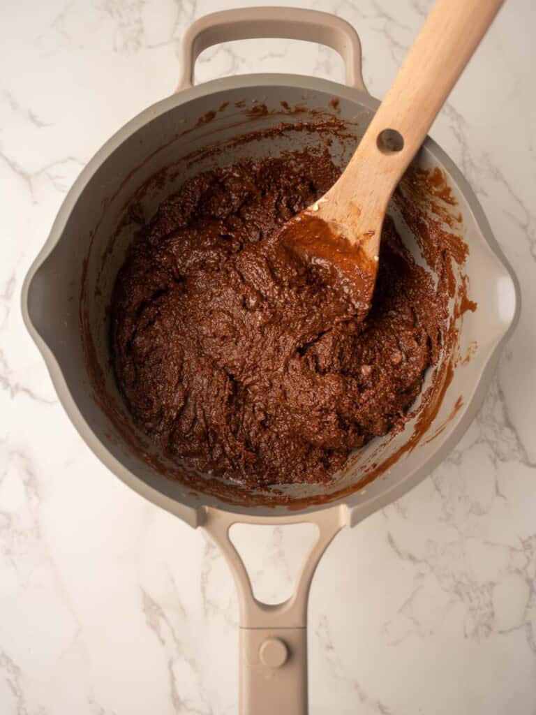 Saucepan filled with the melted chocolate mixture for rocky road with Maltesers, stirred together with a wooden spoon.