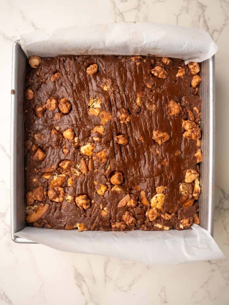Tray of rocky road with Maltesers pressed into a parchment-lined tin, showing the chocolate mixture studded with biscuit pieces.