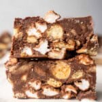 Close-up of two thick slices of rocky road with Maltesers, showing chocolate, biscuit pieces, and mini marshmallows packed together in a fudgy bar.