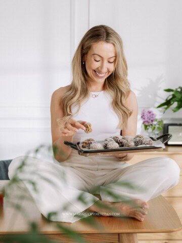 Dietitian smiling while holding a tray of healthy homemade PCOS-friendly snacks in a bright kitchen.