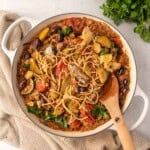 Sardines puttanesca pasta with courgette, artichoke hearts, olives, capers and tomato sauce in a skillet topped with fresh parsley