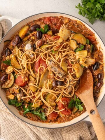 Sardines puttanesca pasta with courgette, artichoke hearts, olives, capers and tomato sauce in a skillet topped with fresh parsley