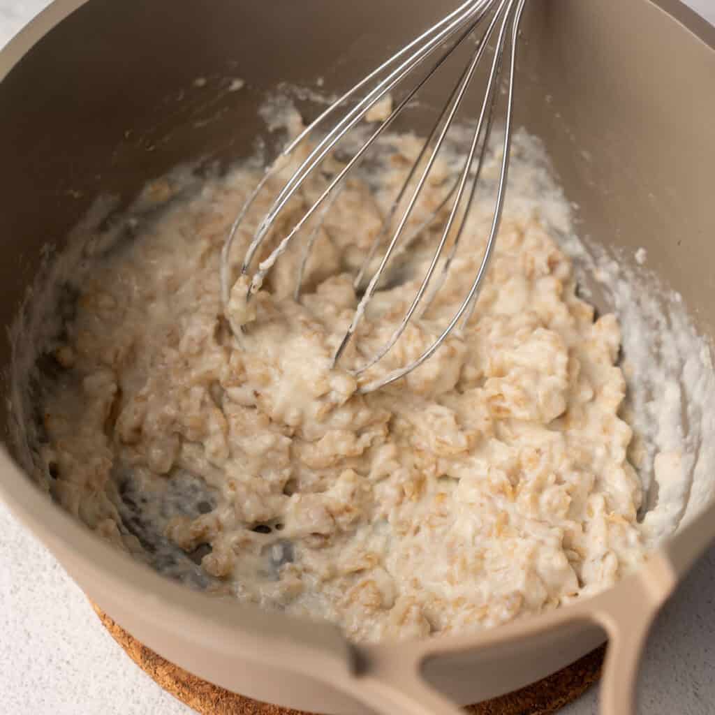 A whisk stirring creamy cooked high protein oatmeal in a pot, showing the thick texture as it comes together.