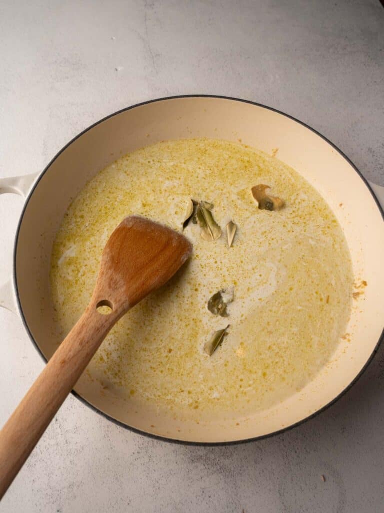 Light coconut milk poured into Thai green curry paste with kaffir lime leaves in a large pot.