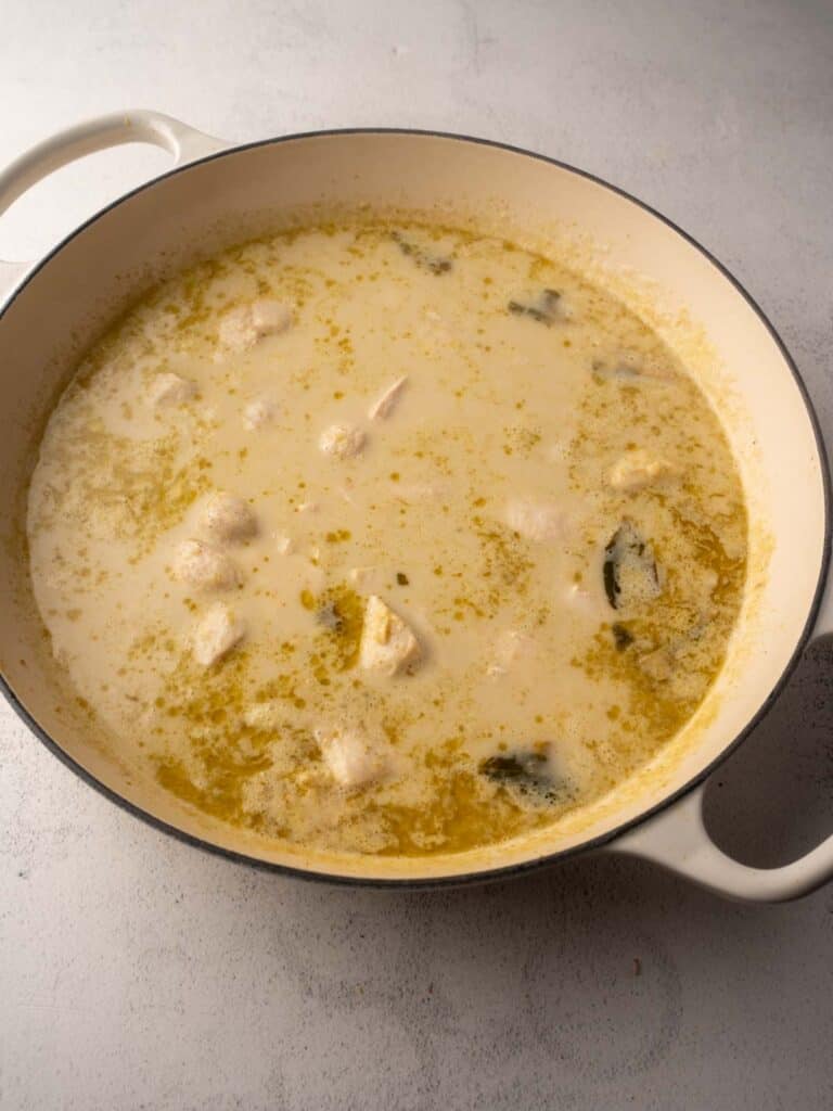 Chicken pieces simmering in a light coconut Thai green curry sauce in a large pot.