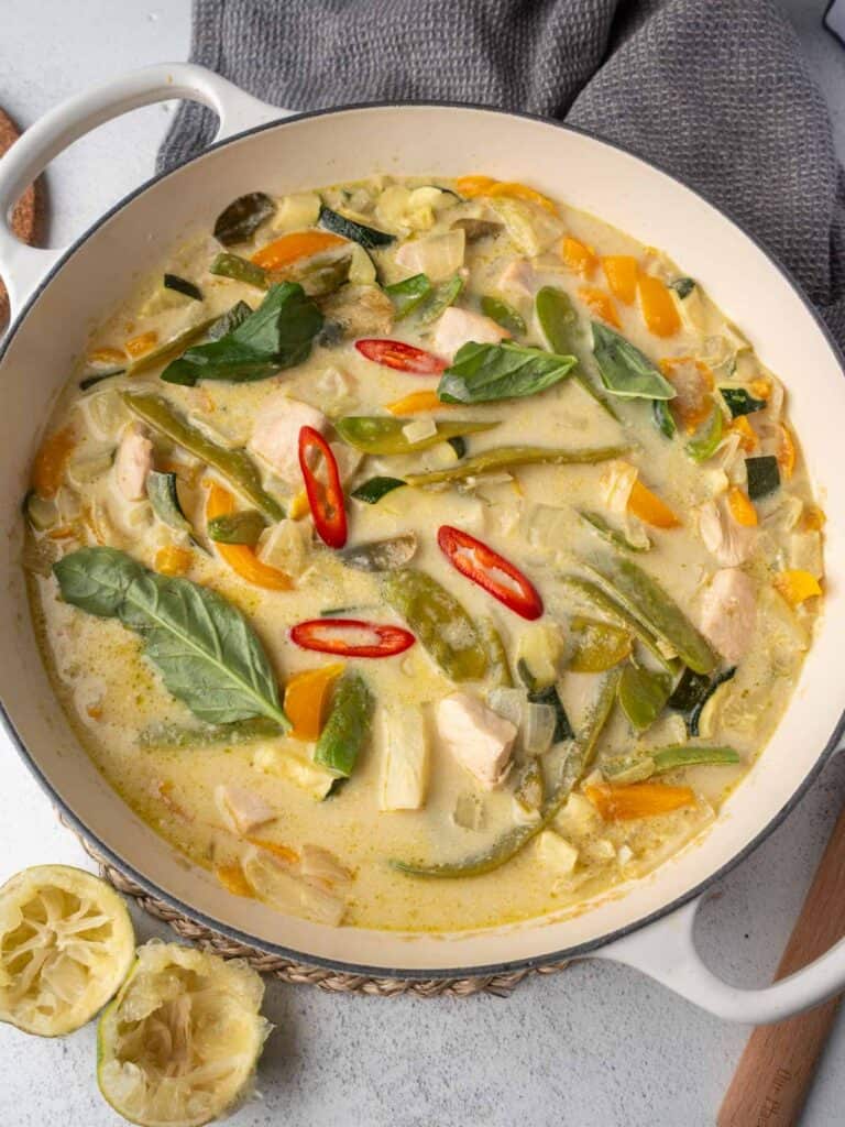 Lightened-up Thai green chicken curry with vegetables, basil, and sliced red chili in a cream-colored pot.