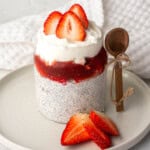 Chia seeds and yogurt pudding layered with strawberry compote and topped with fresh sliced strawberries in a glass jar.