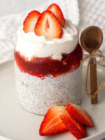 Chia seeds and yogurt pudding layered with strawberry compote and topped with fresh sliced strawberries in a glass jar.