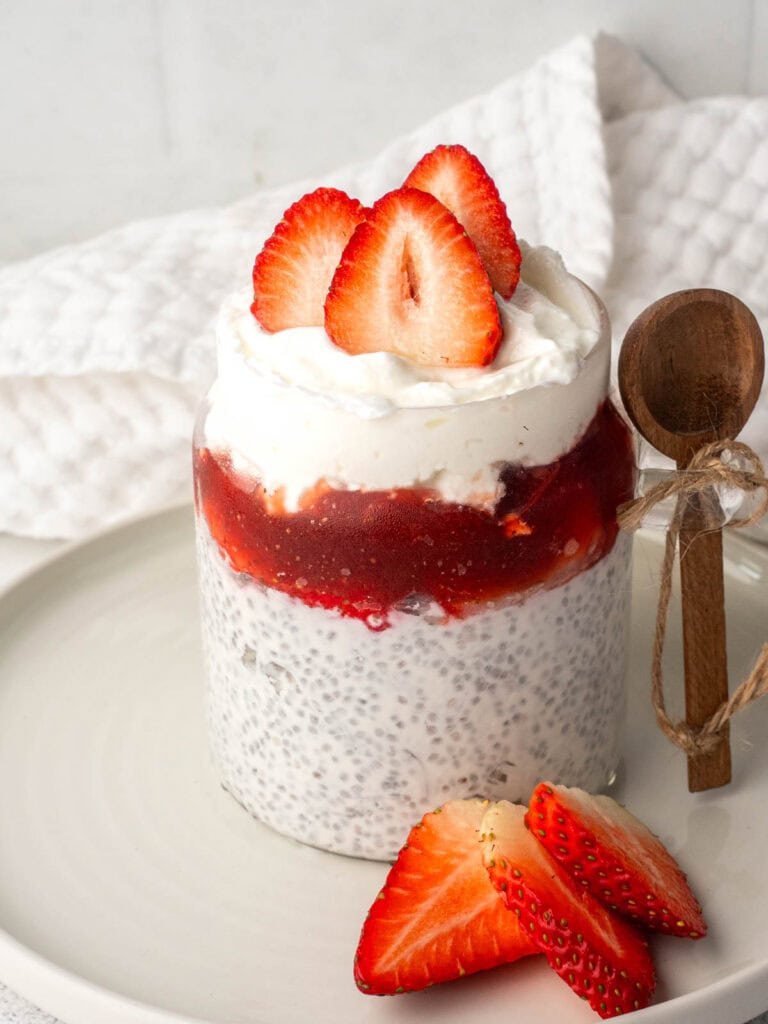 Chia seeds and yogurt pudding layered with strawberry compote and topped with fresh sliced strawberries in a glass jar.