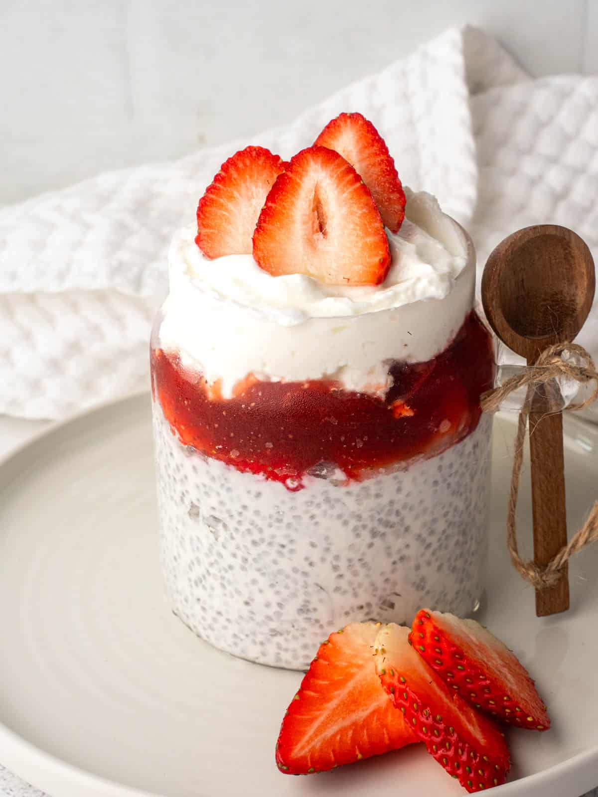 Chia seeds and yogurt pudding layered with strawberry compote and topped with fresh sliced strawberries in a glass jar.