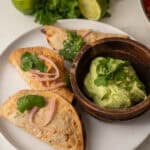 Chicken mini tacos on corn tortillas topped with pickled onions and fresh cilantro, served with a bowl of creamy guacamole.