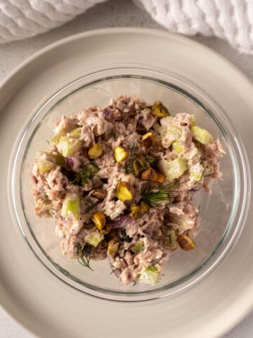 Healthy tuna salad recipe made with Greek yogurt, feta, pistachios, celery, red onion, and fresh dill, served in a glass bowl.