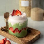 Strawberry matcha overnight oats layered in a glass jar with green matcha oats, sliced strawberries around the sides, and a creamy strawberry yogurt topping.